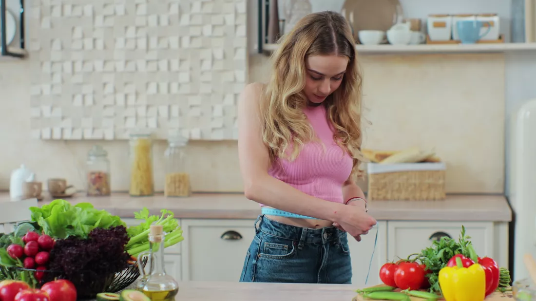 young-girl-measures-her-waist-kitchen-near-table-with-vegetables-fruits-concept-healthy-eating-diet