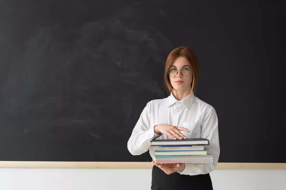 portrait-happy-teacher-standing-front-black-board-holding-stack-books-her-hands