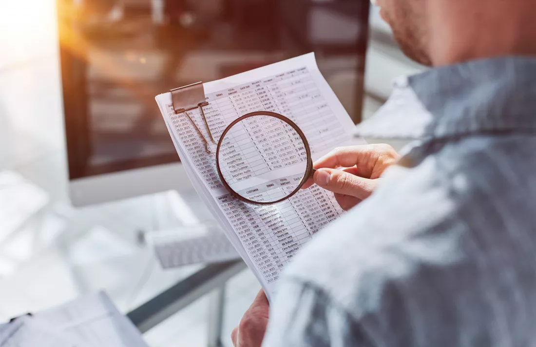 man-looking-through-magnifying-glass-documents-notebook